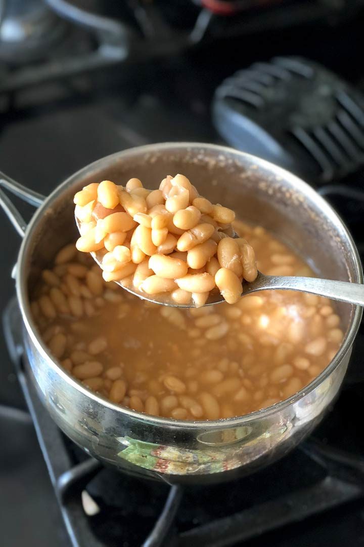 Spoon holding up cooked beans over a pot on black stove.