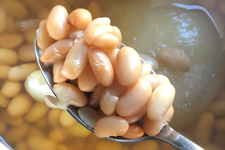 Fully cooked beans closeup with bean stock and cooked onion behind it.