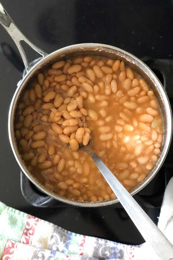 Overhead view of large pot of frijoles de la olla beans with long spoon on black stovetop.